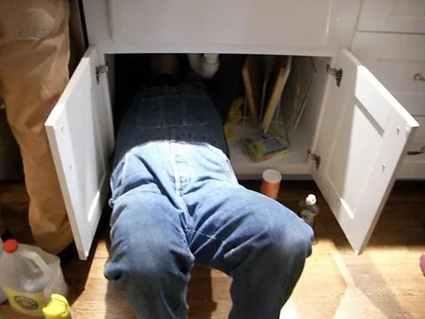 Plombier travaillant sous un évier de cuisine